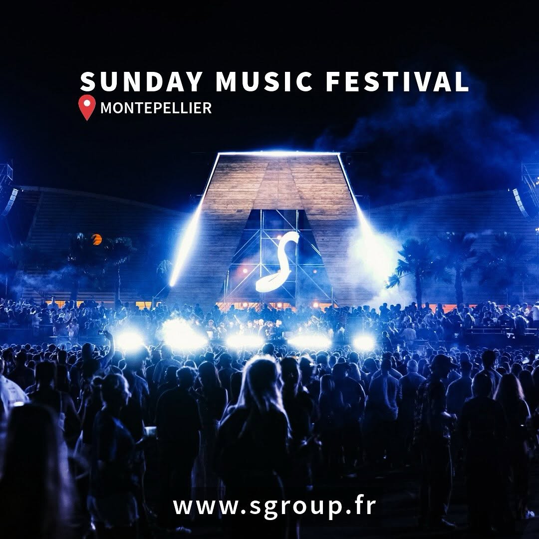 Outdoor festival main stage with a wooden archway lit in blue, stage smoke and a large night crowd.