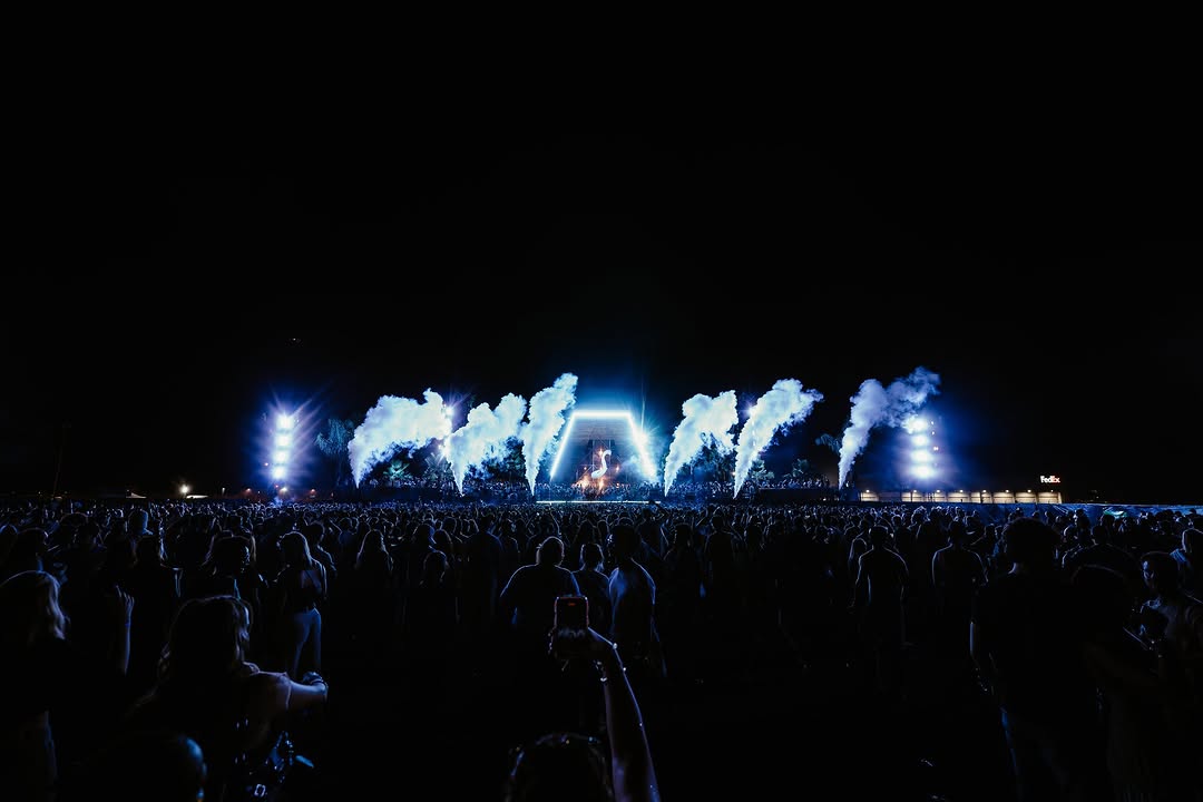 Wide night view of a festival stage, blue smoke plumes either side of a central archway, crowd in the foreground.
