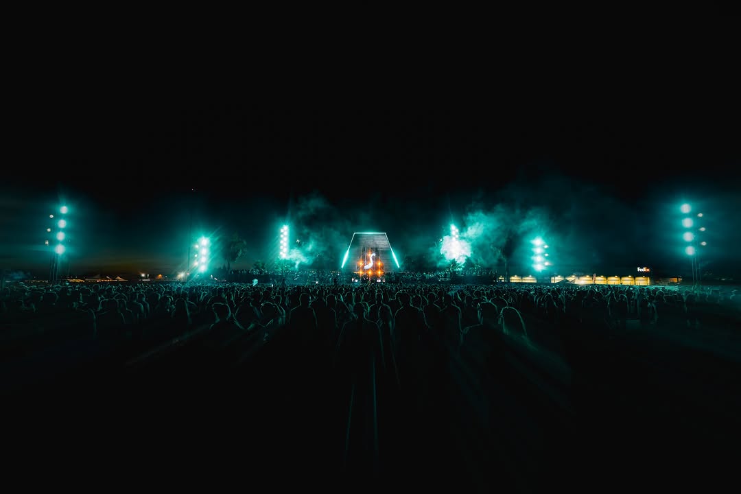 Night festival stage lit in emerald green, central archway with vertical beams, crowd in the foreground.